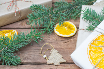 Christmas presents or gift box wrapped in kraft paper with decorations, pine cones, dry orange orange slices and fir branches on a rustic wooden background. Holiday concept
