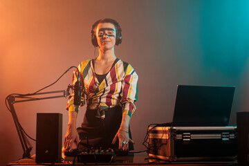 Happy female performer working as dj with turntables, mixing techno music with bass and audio...