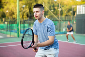 Young teenage tennis player training on court. Boy using racket to hit ball.