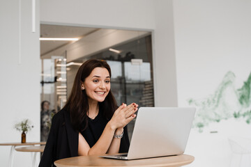 Fototapeta na wymiar Cheerful surprised woman smile and looking at amount of income earnings salary and rejoices. Happy girl rejoices in winning and sitting in front of laptop in white cafe.