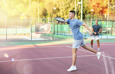 Obraz premium Young teenage tennis player training on court with male partner. Boy using racket to hit ball.