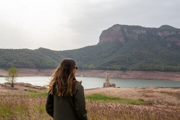 woman from the back looking at a reservoir with little water due to the drought and the little rain effect of global warming