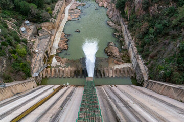 Dam spewing water with great force into a reservoir in the mountains. Dizzying stair access
