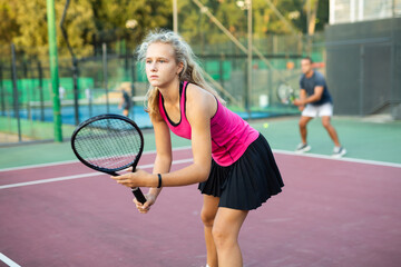 Focused young woman playing tennis on court, preparing to hit forehand to return ball. Concept of sport training