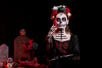 Scary goddess of dead with black costume and catrina skull body art, wearing flowers headband with roses. Celebrating dios de los muertos mexican tradition on halloween in studio.