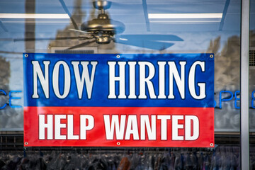 Now Hiring Help Wanted Sign in window of business with ceiling fan visible inside