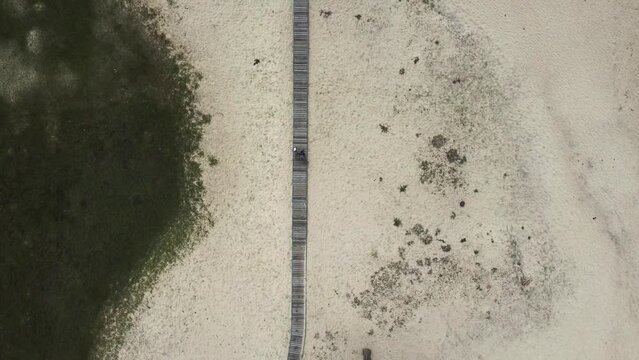 4k Top view of tourists walk along pier on sandy island in summer irrl. Aerial pic of people walking together on isle and traveling outdoors. Operator launches drone and takes pictures of strolling