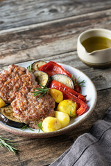 Grilled cutlets and salad of vegetables potatoes zucchini red pepper rosemary on wooden background with linen napkin. Dinner menu with text space