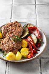 Fried cutlets and salad of grilled vegetables potatoes zucchini red pepper rosemary on gray tile background with cutlery. Dinner menu