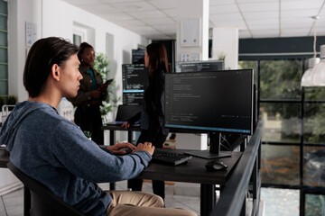 App engineer looking at computer typing machine learning server code, sitting at desk in software...