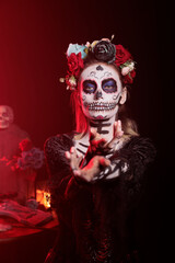Creepy horror woman reaching with hand, trying to lure and tempt victims in studio. Flirty santa muerte model with mexican ritual costume on holiday celebration, day of the dead myth.