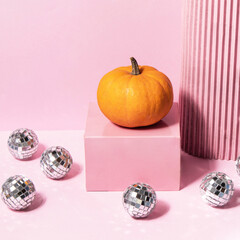 Creative Halloween party idea. Pastel autumn concept. Little pumpkin and disco balls on light pink background. Minimalistic fall composition.