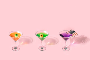 Spooky Halloween concept. Colorful cocktails with eyeballs and spider on pastel light pink background. Creative festive idea. Minimalistic holiday party composition with copy space.