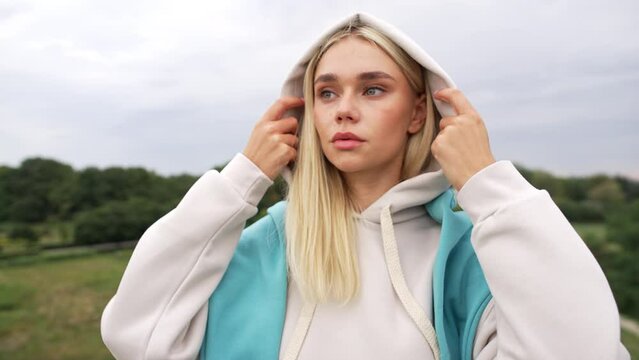 Caucasian beautiful woman puts on a hood. The girl in the sports hoodie is serious and purposeful. High quality 4k footage