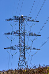 Electrical transmission tower on the top of a hill against a cloudless blue sky.