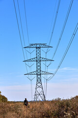 An electrical transmission tower with a distant figure walking