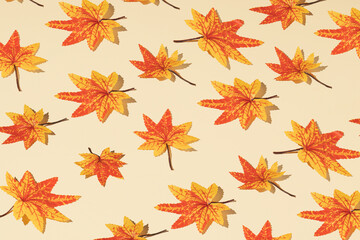 Autumn pattern made of orange and yellow leaves against a beige background. Minimal season nature concept.