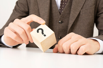 a business man's hand holds a wooden cube block with question marks on the corner. concept of financial, rating and mortgage rates