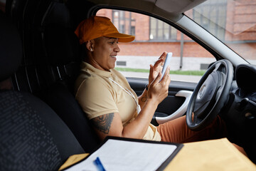 Side view portrait of female delivery driver using smartphone app in van