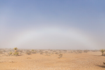 Winter weather phenomenon fog bow or white rainbow caused by sunlight meeting moisture and refracting light captured on cold December day within the Mojave desert