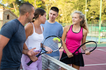 Happy four male and female partners of tennis emotionally talking at tennis court