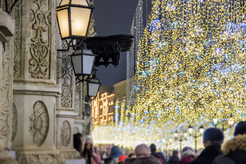 People and tourists walk along street decorated for New Year and Christmas