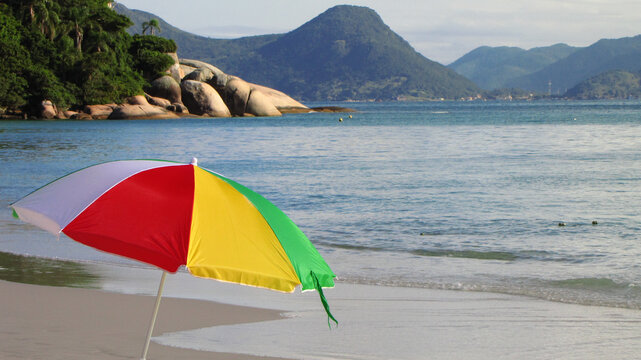 colorful beach umbrella with sea, stones and mountain on background - Summer in Florian&oacute;polis, Brazil 
