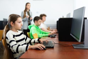 Young girl sitting at table and using computer during lesson.