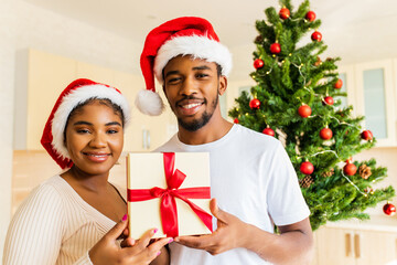 Obraz na płótnie Canvas afro american couple giving gift box to each other in house near christmas tree
