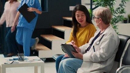 Diverse elderly women analyzing checkup report on digital tablet and papers, filling in medical form before attending examination at health center. Talking about diagnosis and treatment.