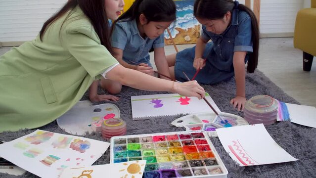 Asian two siblings learning study watercolor paint together at home. Teacher or parent teach student or daughter drawing paint color imagination on paper homework.Activity creativity education concept
