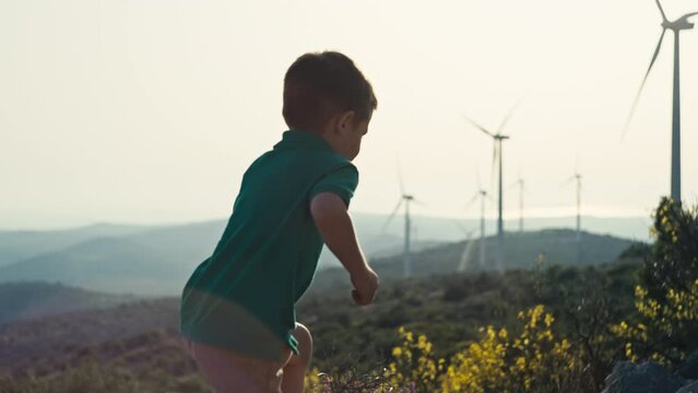 A boy runs near a windmill farm. The concept of a child and environmental protection, wind energy, environmentally friendly electricity, protection of the planet. High quality 4k footage