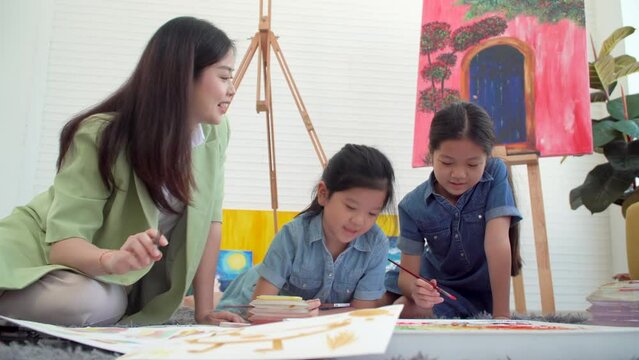 Asian two siblings learning study watercolor paint together at home. Teacher or parent teach student or daughter drawing paint color imagination on paper homework.Activity creativity education concept