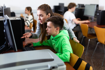 Teacher helping teenage boy to solve computer problem during lesson.