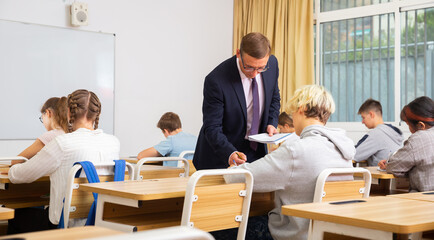Fototapeta na wymiar Group of focused teenage students sitting at classroom working at class with helpful teacher