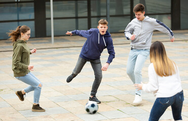 Teen friends spending time together outdoors playing with ball on square near school