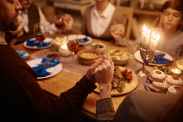 Close up of Jewish couple holding hands during family prayer at dining table on Hanukkah.