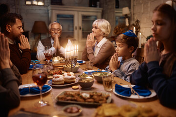 Multigeneration Jewish family praying at dining table on Hanukkah.