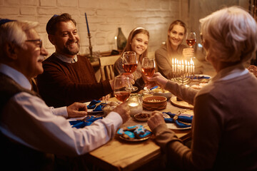 Happy man toasting with his family during dinner at dining table on Hanukkah.