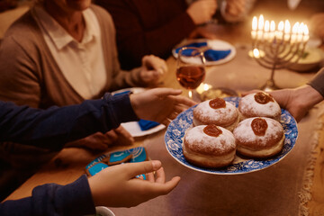 Close up of Jewish mother and daughter passing traditional jam filled donuts during family meal on...