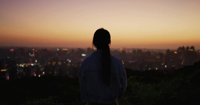 Back rear view of woman look at the city under sunset