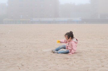 Expressive young girl is playing on the beach on a very foggy day