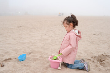 Expressive young girl is playing on the beach on a very foggy day