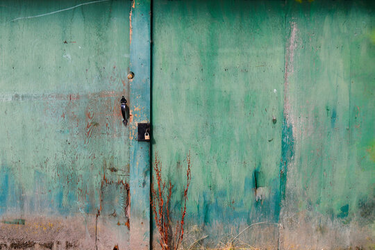 A large closed and locked wooden gate with green and blue weathered paint. 