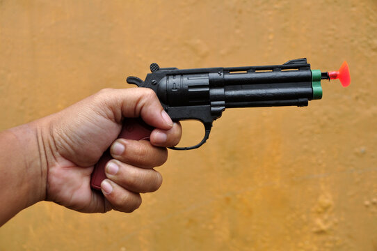 Hand holding toy gun on yellow wall background