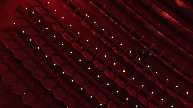 Rotating drone shot of a woman walking down a row in a theatre with a torch looking for her seat