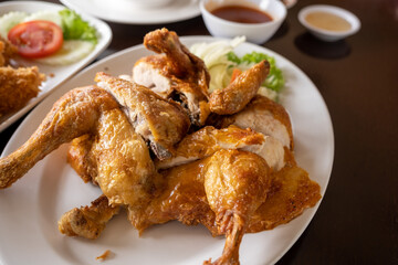 The whole fried chicken is chopped into pieces and placed in a white plate placed on the table.