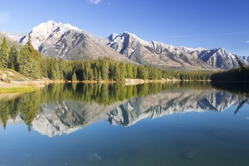 
Mountain Range and Green Forest Trees Reflected in Calm Lake Water. Blue Sky Scenic Autumn Landscape Banff National Park, Canadian Rocky Mountains