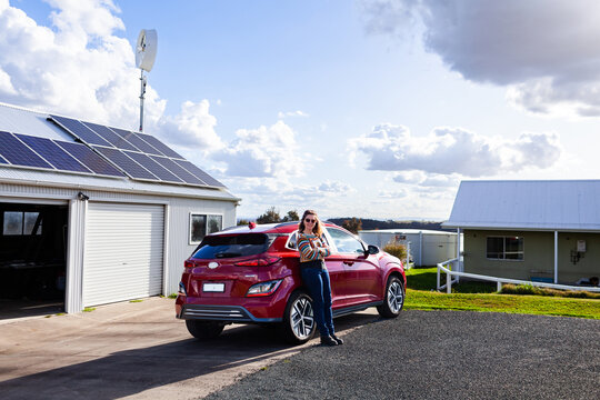 happy middle age woman standing with electric vehicle car and solar panels - sustainable living
