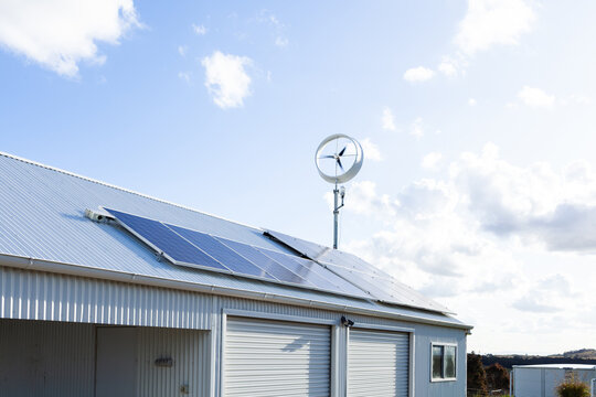 Off grid sustainable living with wind turbine power generator and solar panels on shed roof